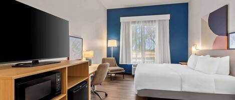 A hotel room with a bed, a desk with a chair, a television, a microwave, and a lamp.