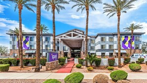 A hotel with a modern architectural design, featuring a central entrance with a red carpet, surrounded by palm trees and well-maintained landscaping.