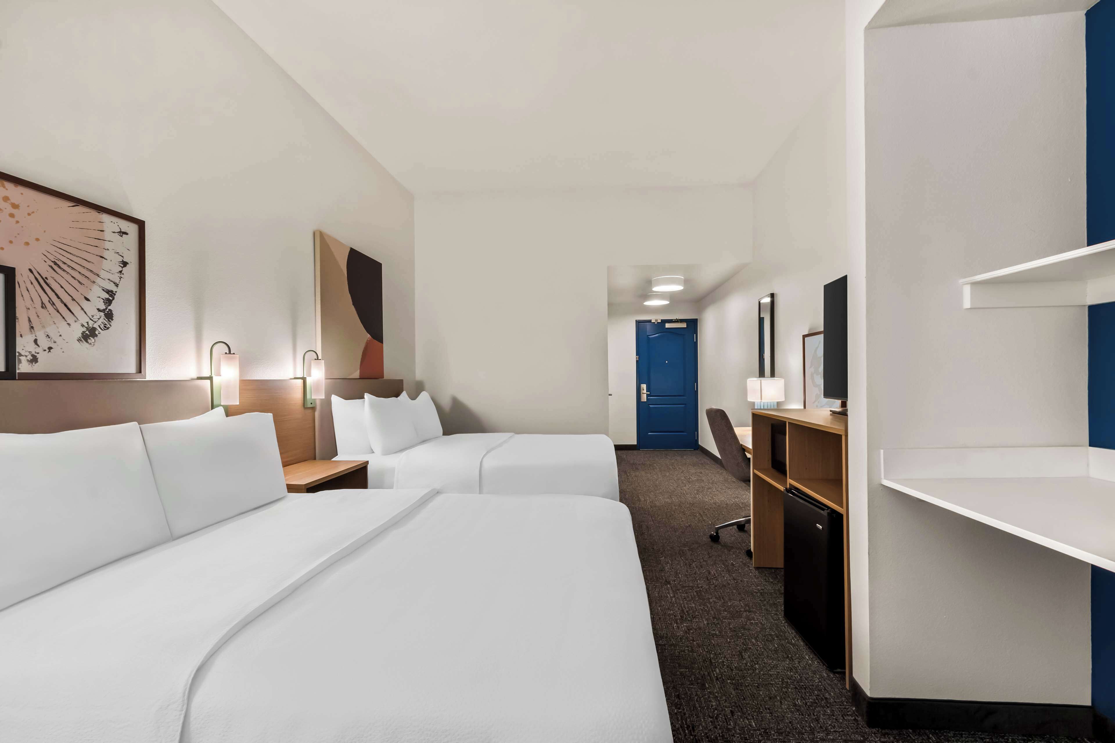 A hotel room with two beds, a desk, a chair, a wardrobe, and a bathroom door.