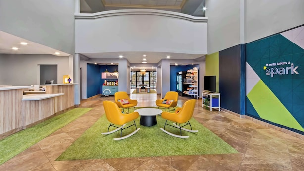 A lobby with a reception desk, a seating area with chairs, a chandelier, and a wall with the text "It only takes a spark".