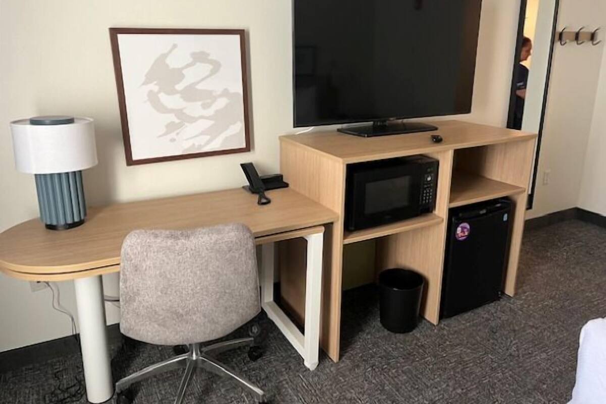 A hotel room with a desk, a television, a microwave, and a trash bin.