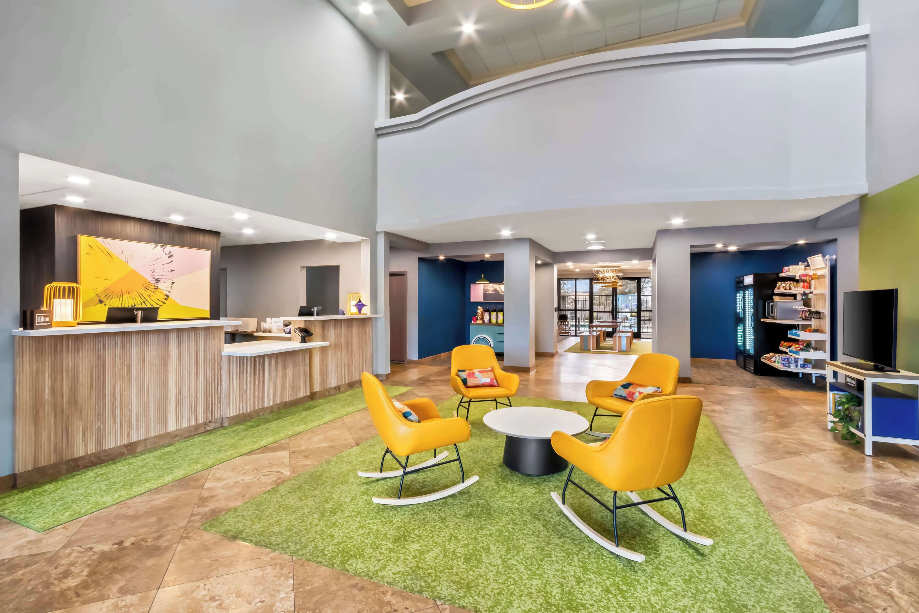A spacious lobby with a reception desk, seating area with yellow chairs, and a children's play area.