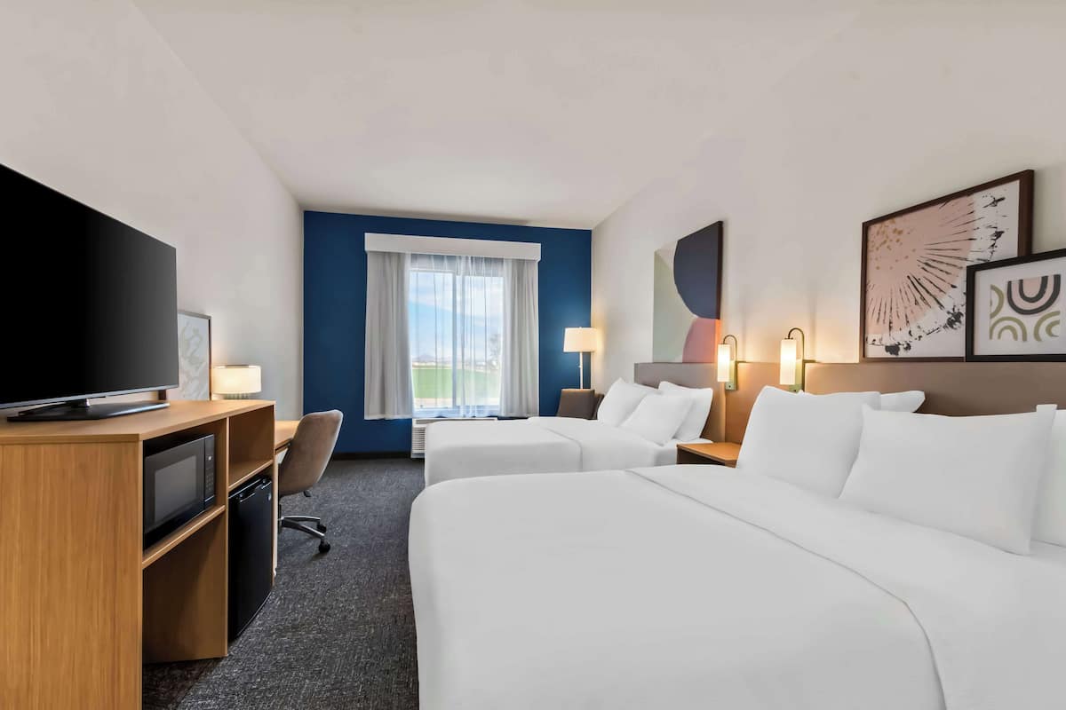 A hotel room with two beds, a desk with a TV, a desk lamp, and a window with curtains.