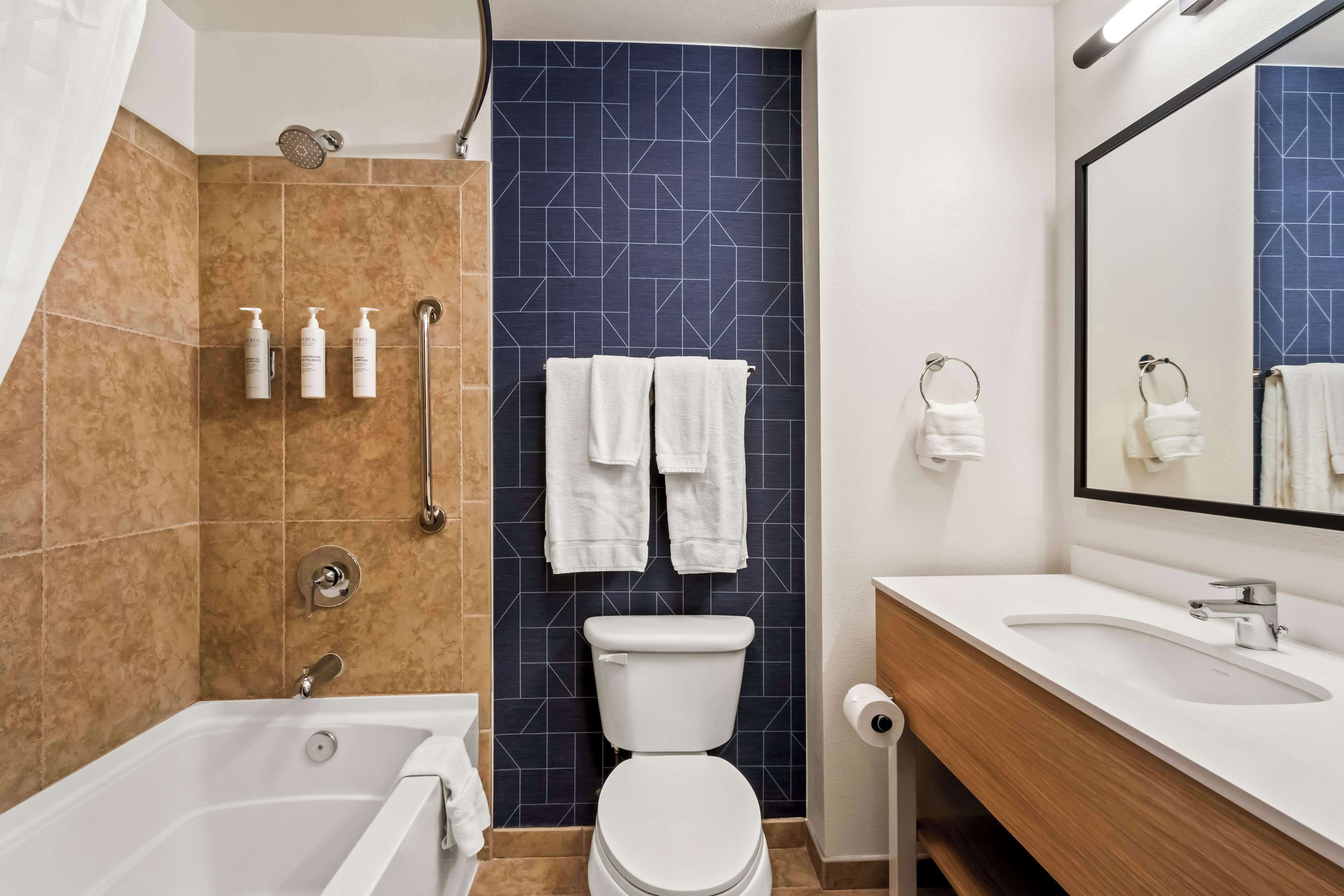A modern bathroom with a bathtub, toilet, and sink. There are towels hanging on a rack, and toiletries on the wall.