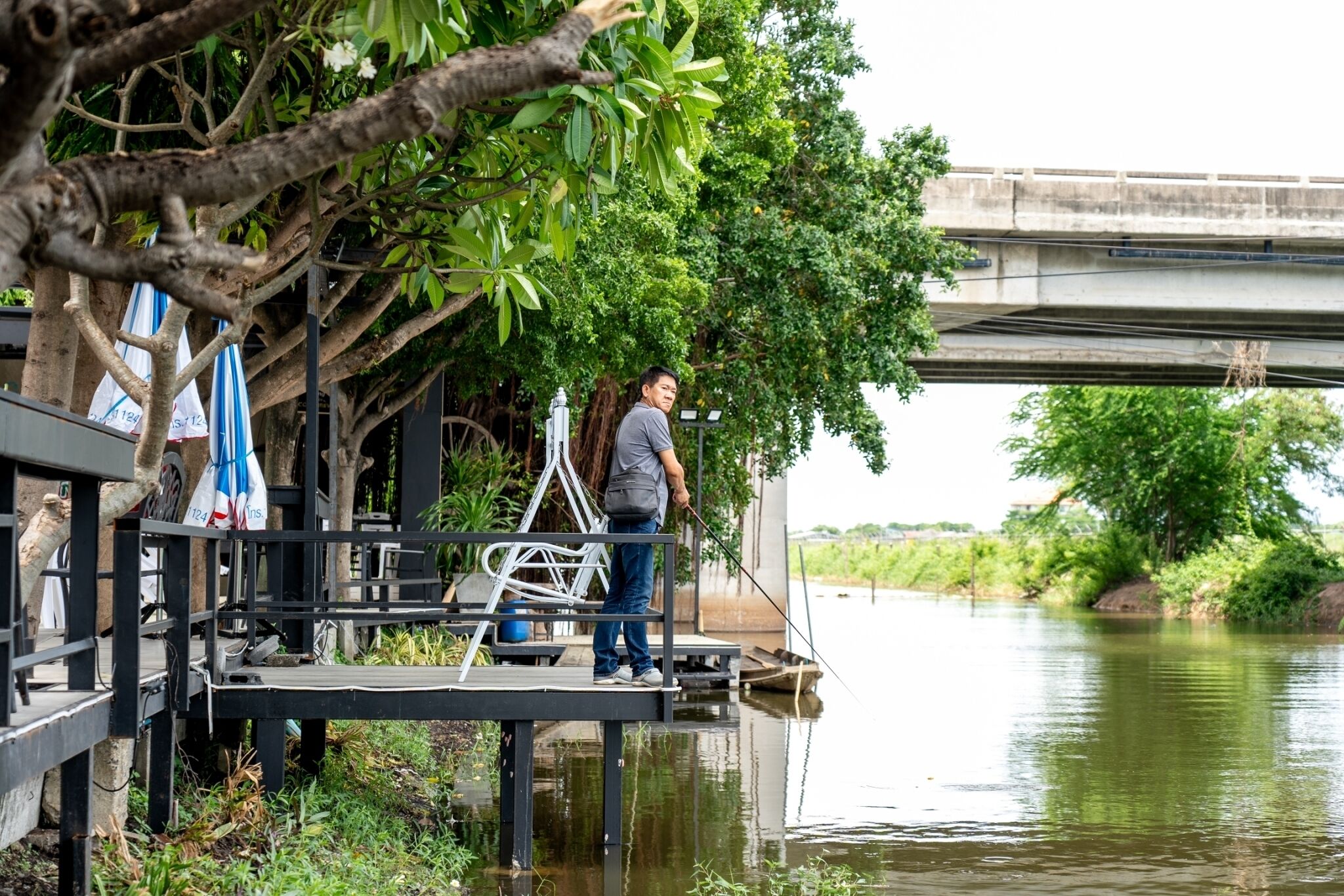 A person standing on a dock by a river, with a bridge in the background.