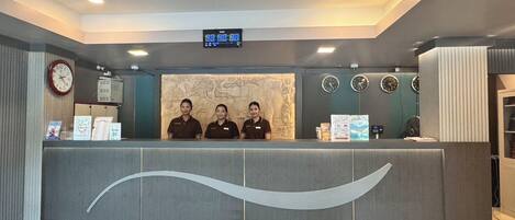 A reception desk with three staff members, a digital clock, and multiple wall clocks.