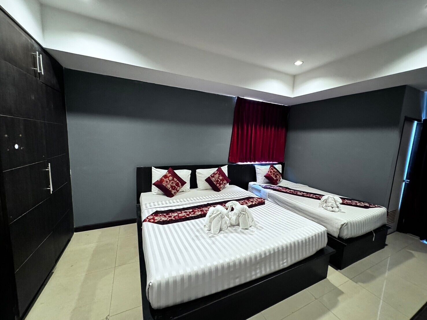 A modern hotel room with two beds, dark walls, and a red curtain.