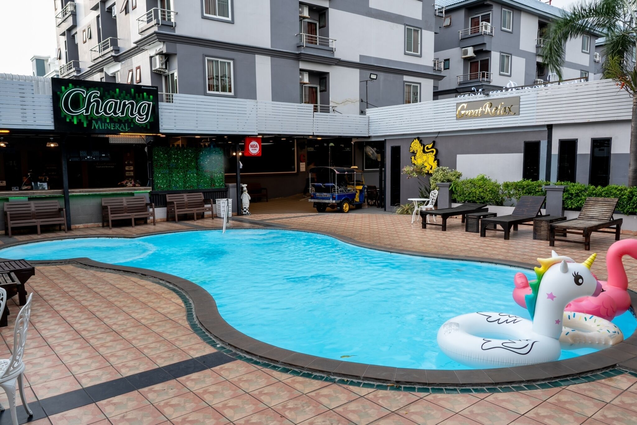 A swimming pool with inflatable swan and unicorn floats, surrounded by lounge chairs and a restaurant named 'Chang Minerals'.