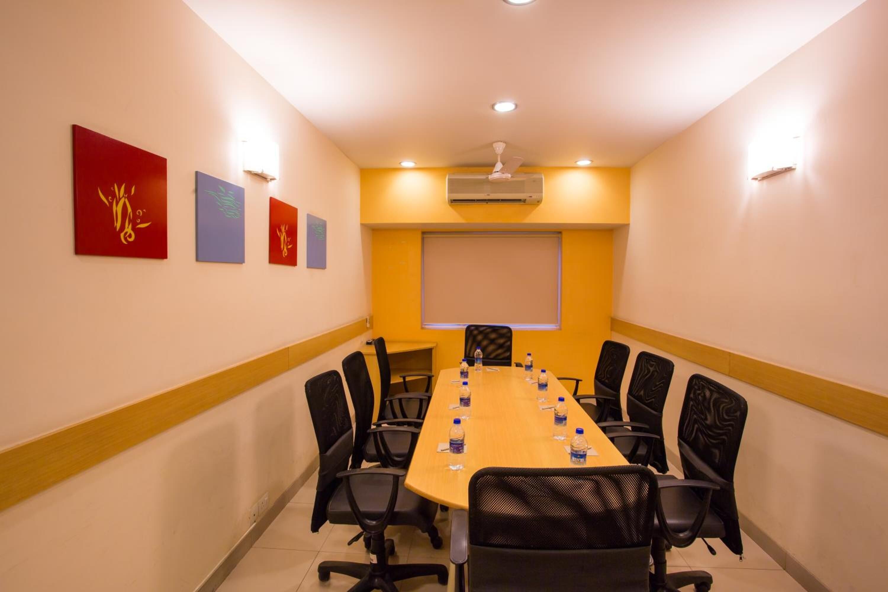 A conference room with a long table, black chairs, and a projector screen on the wall.
