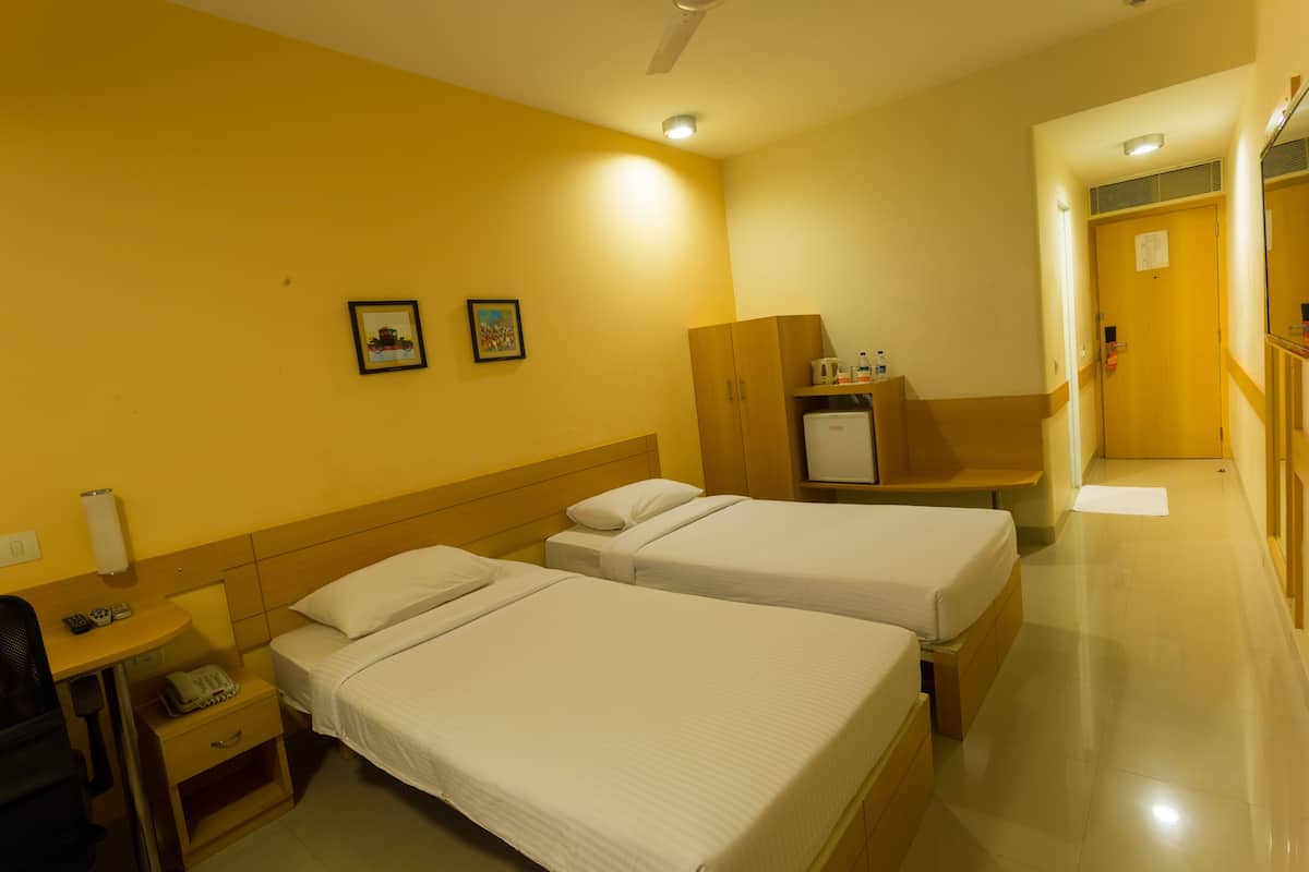 A hotel room with two single beds, a desk with a chair, a small table with a telephone, and a cabinet.