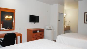 Habitación de hotel con dos camas, un escritorio, una silla, un televisor, un microondas y un baño pequeño con espejo y toallero.