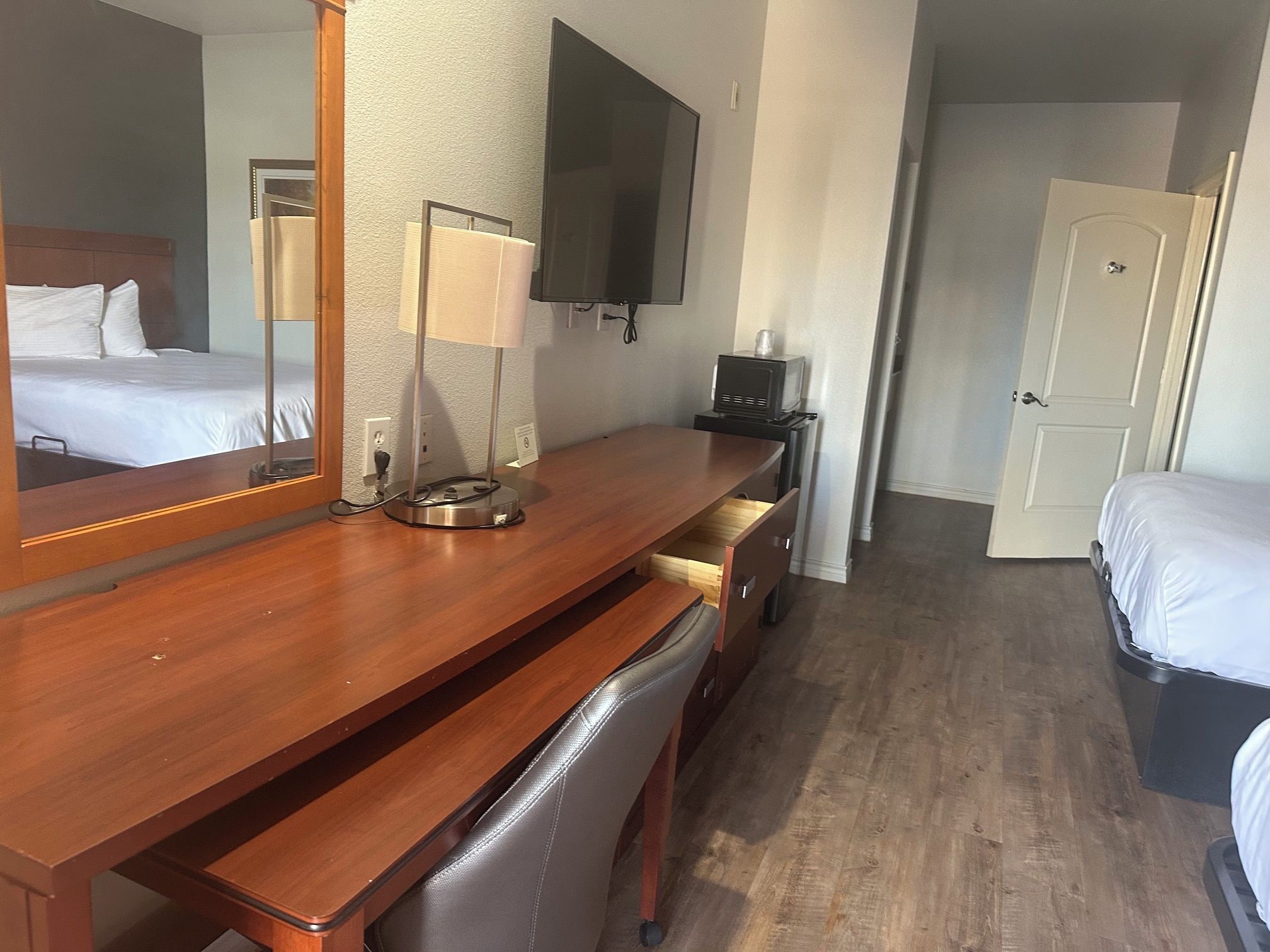 A hotel room with a wooden desk, a chair, a television, a lamp, and a bed.