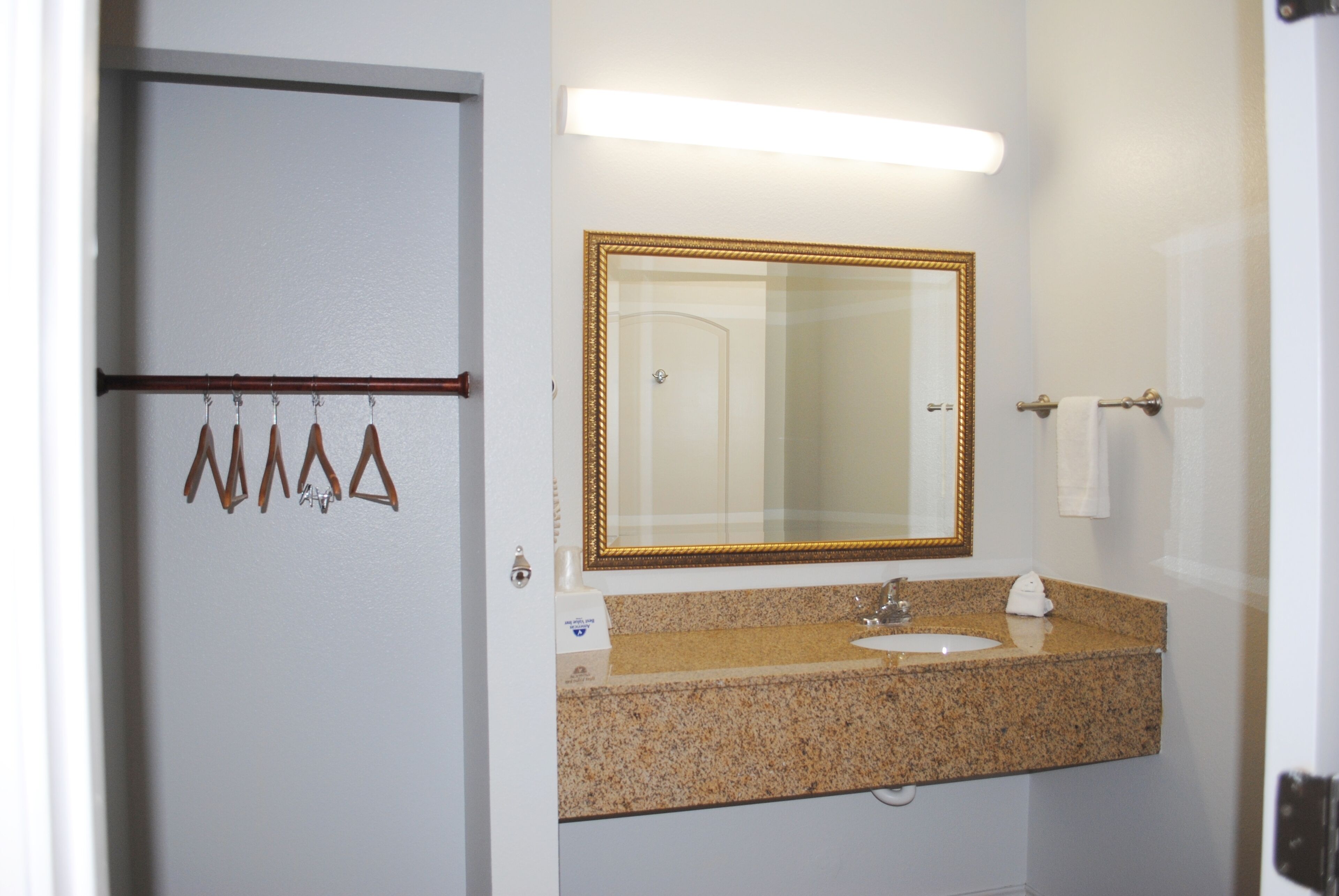 A bathroom with a granite countertop, a gold-framed mirror, and a towel rack with towels.