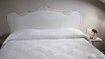 A neatly made bed with a white headboard and a small bedside table with a vase of red flowers.