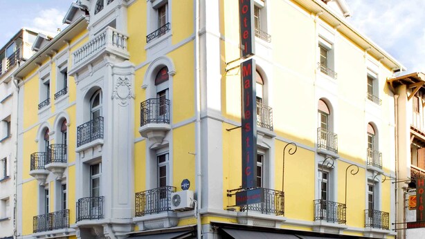 A yellow and white building with balconies, a restaurant named "Le Majestic," and a sign for "Hotel Majestic." - Majestic (Lourdes)