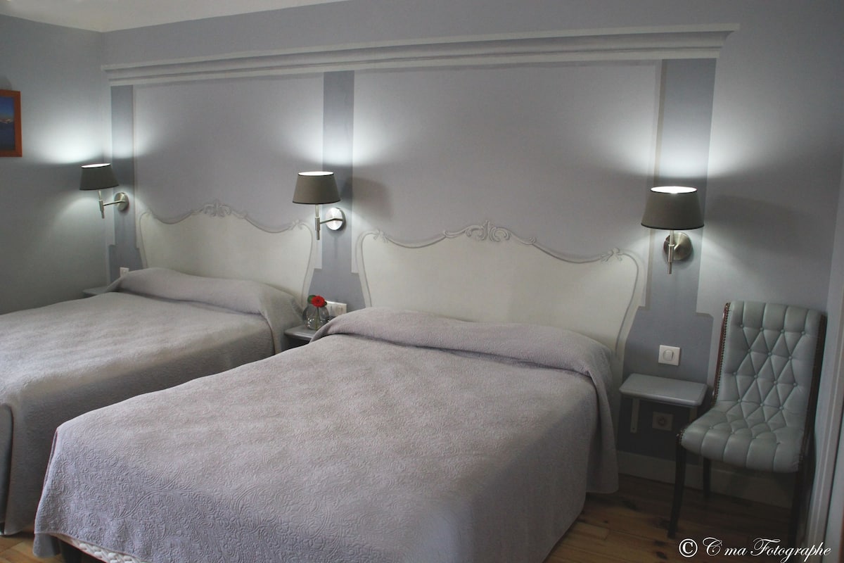 A hotel room with two beds, a chair, and two wall-mounted lamps.