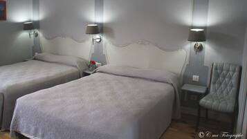 Una habitación de hotel con dos camas, una silla y dos lámparas fijadas a la pared.