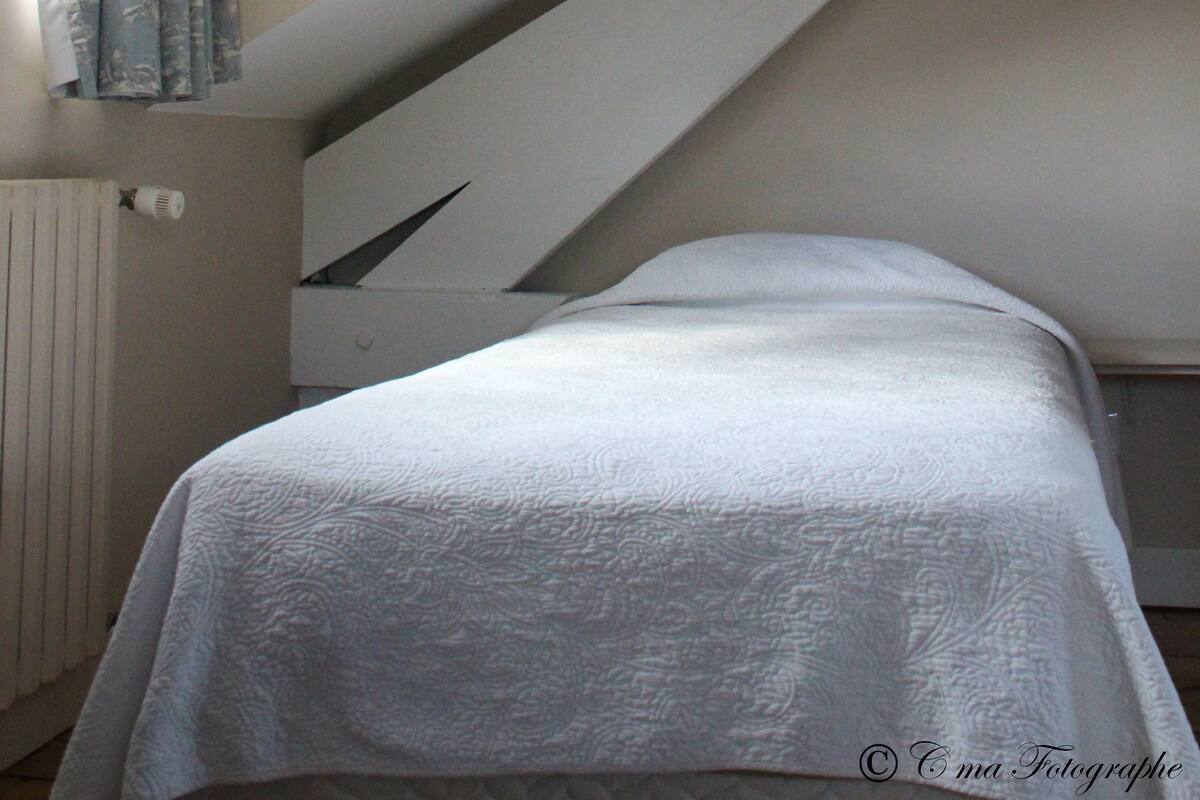 A bedroom with a sloped ceiling, a radiator, and a window with curtains.