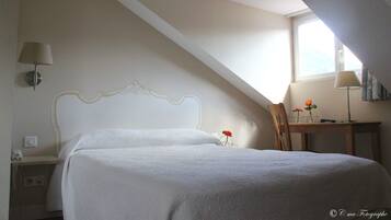 A bedroom with a bed, a desk, and a chair. There is a window providing natural light.