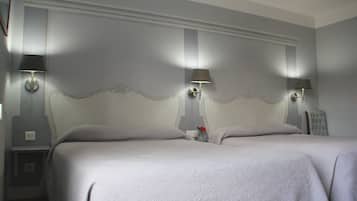 A hotel room with two beds, a nightstand, a lamp, and a vase with flowers.