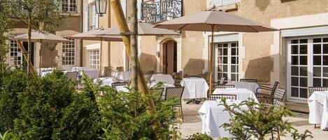 An outdoor dining area with tables and chairs, surrounded by greenery.