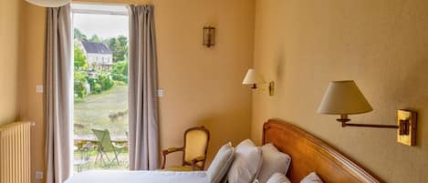 A hotel room with a large bed, a view of the outdoors, a chair, and a lamp.