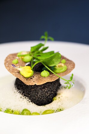 Un dessert composé d’une base de gâteau, de petits pois verts et décoré d’une feuille.