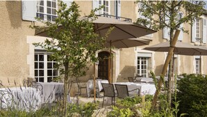 An outdoor patio with tables and chairs, surrounded by plants and trees. - Hôtel Restaurant de la Poste et du Lion d'Or (Vezelay)