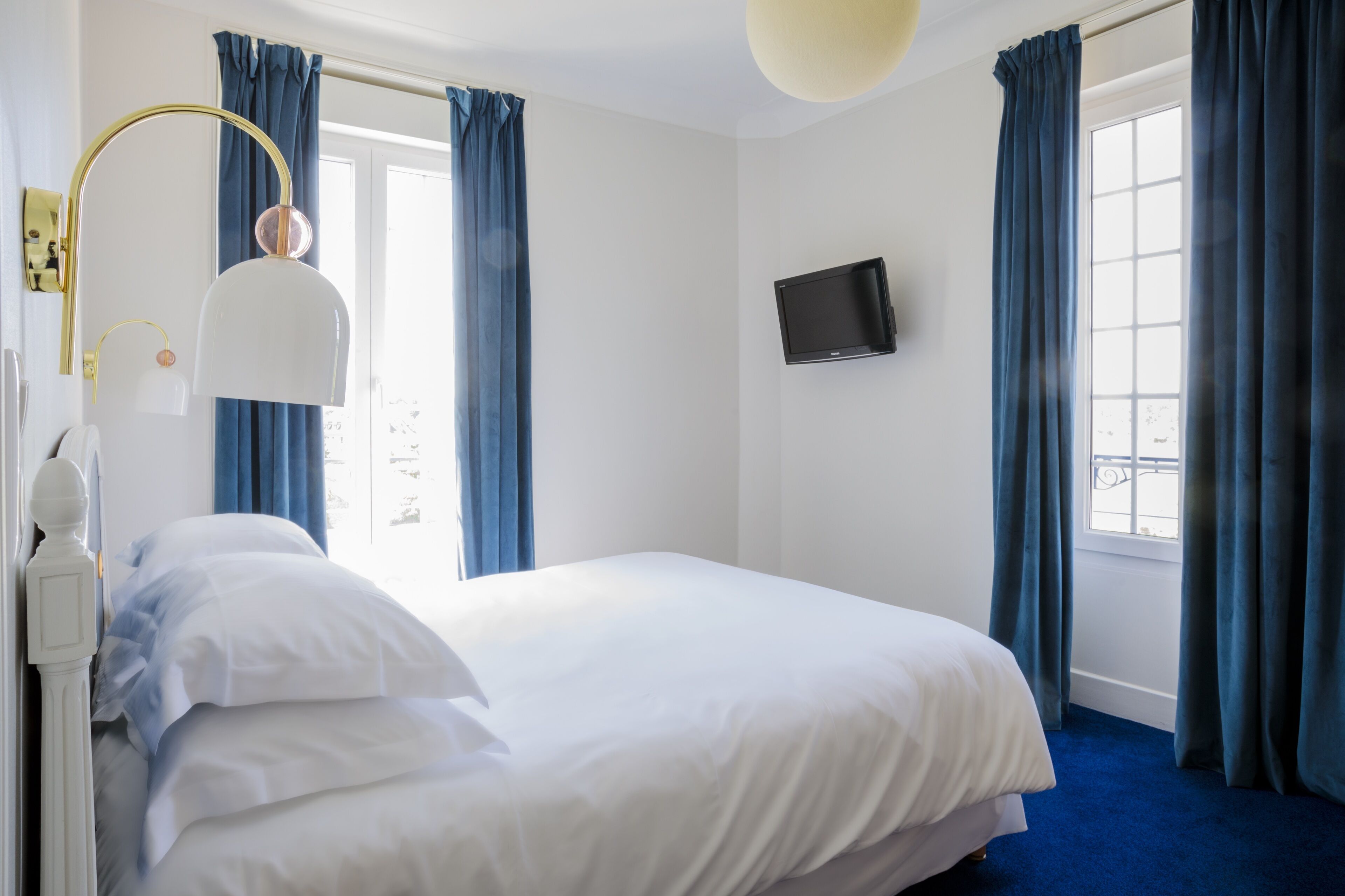 A hotel room with a bed, a TV mounted on the wall, and a window with curtains.