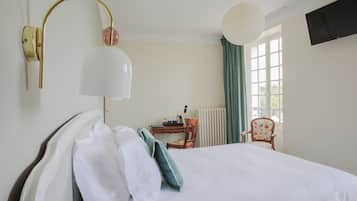Ein Hotelzimmer mit Bett, Schreibtisch, Stuhl, Lampe und einem fenster mit Vorhängen.