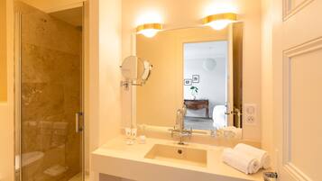 A modern bathroom with a glass-enclosed shower, a large mirror with two wall sconces, and a white sink with toiletries.