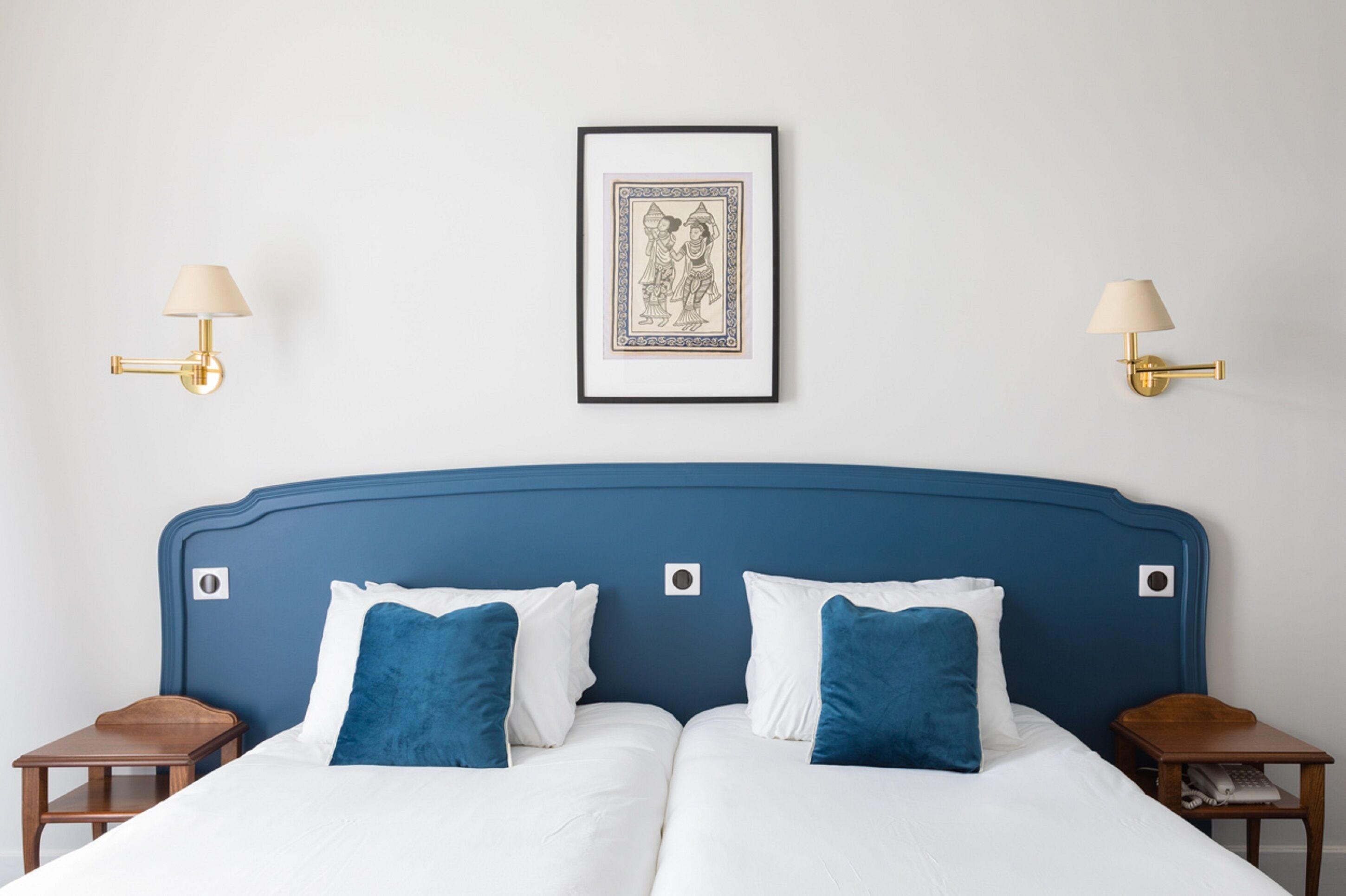 A double bed with white and blue bedding, two bedside tables, and a framed picture on the wall.
