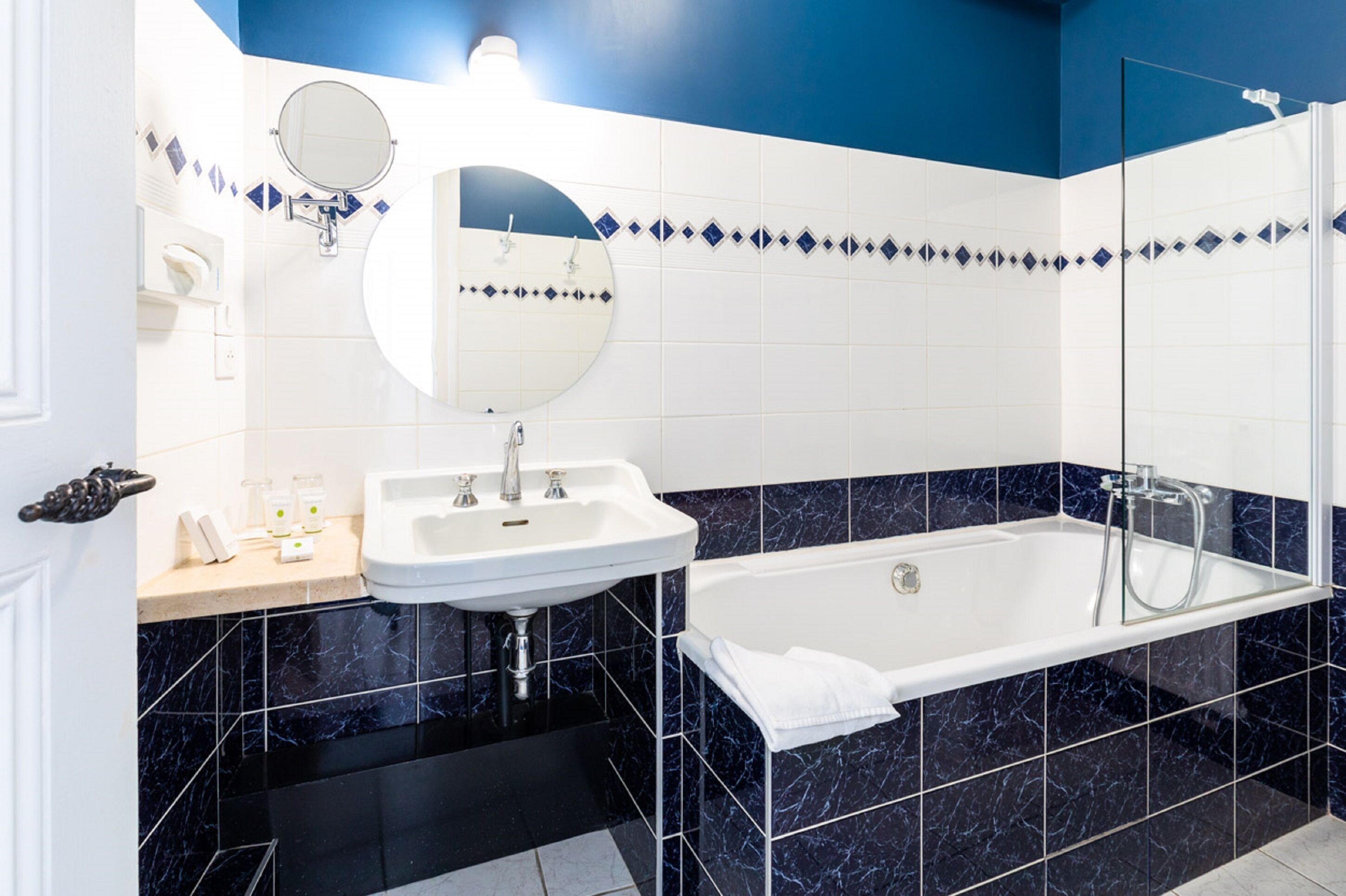 A modern bathroom with a white sink, a round mirror, a bathtub, and blue and white tiled walls.