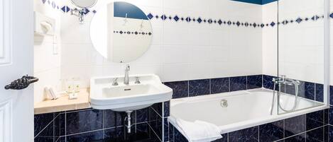 A modern bathroom with a white sink, a round mirror, a bathtub, and blue and white tiled walls.