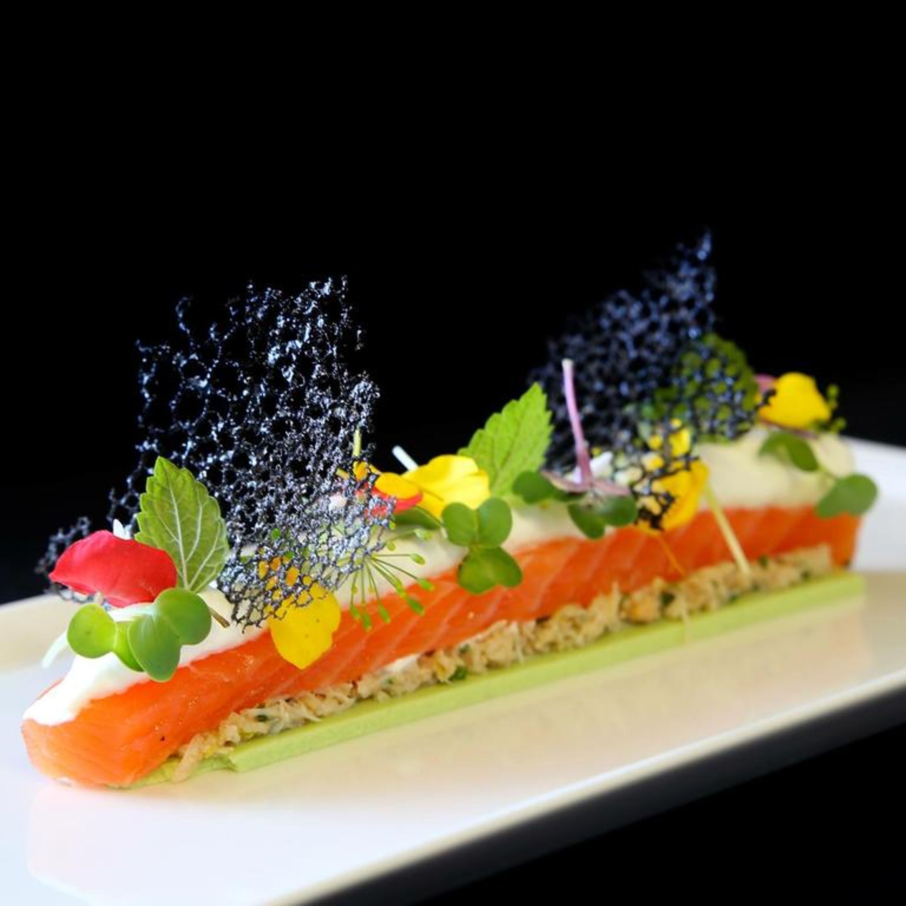 A dish with salmon, greens, and decorative elements.