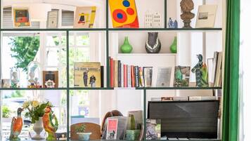 A room with a green-framed bookshelf filled with books, decorative items, and a flat-screen TV. There are two green armchairs and a small wooden table.
