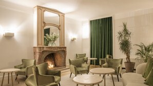 A room with a fireplace, green chairs, round tables, and a mirror. - Hôtel Restaurant de la Poste et du Lion d'Or (Vezelay)
