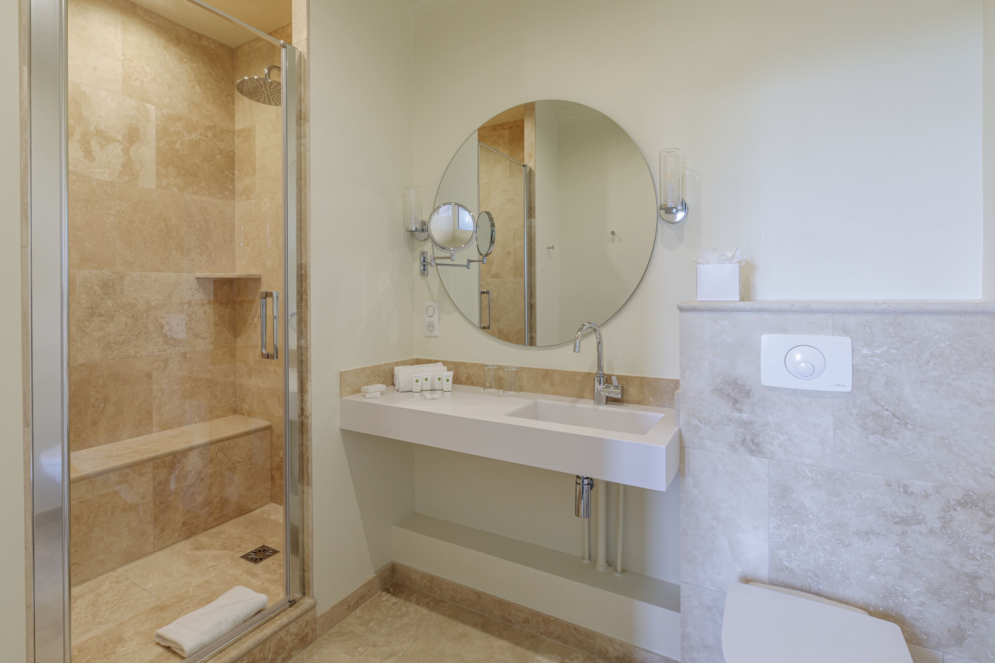 Un baño moderno con ducha de vidrio, un espejo grande, un lavamanos blanco y un inodoro.