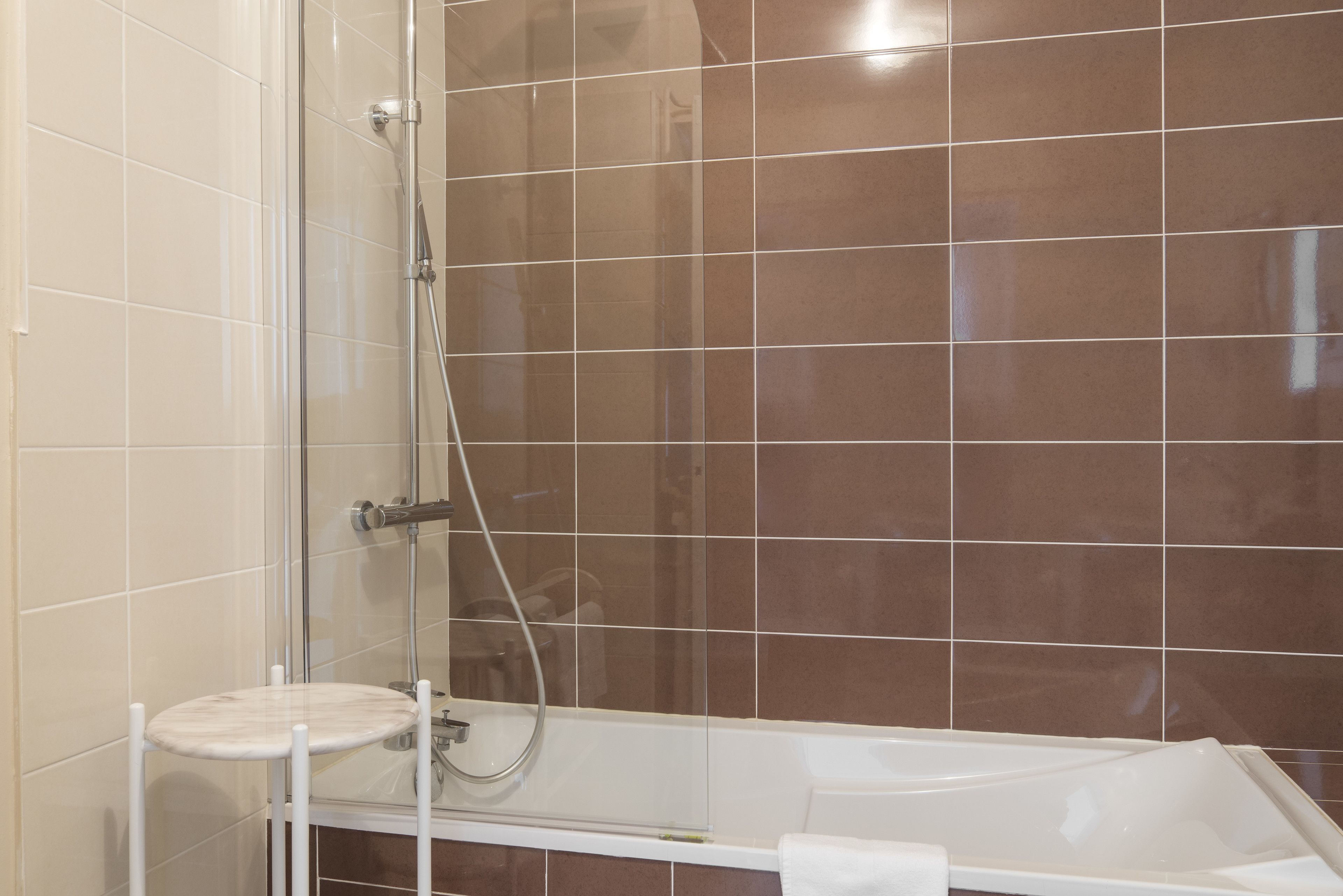 A bathroom with a glass-enclosed shower, a white bathtub, and a small white stool.