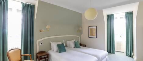 A hotel room with two beds, a chair, a small table, and a hanging light fixture.