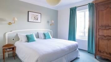 A neatly arranged bedroom with a large bed, two wall-mounted lamps, a framed picture, and a window with curtains.