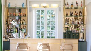A bar area with three bar stools, shelves with liquor bottles, and a window with a view of greenery. - Hôtel Restaurant de la Poste et du Lion d'Or (Vezelay)