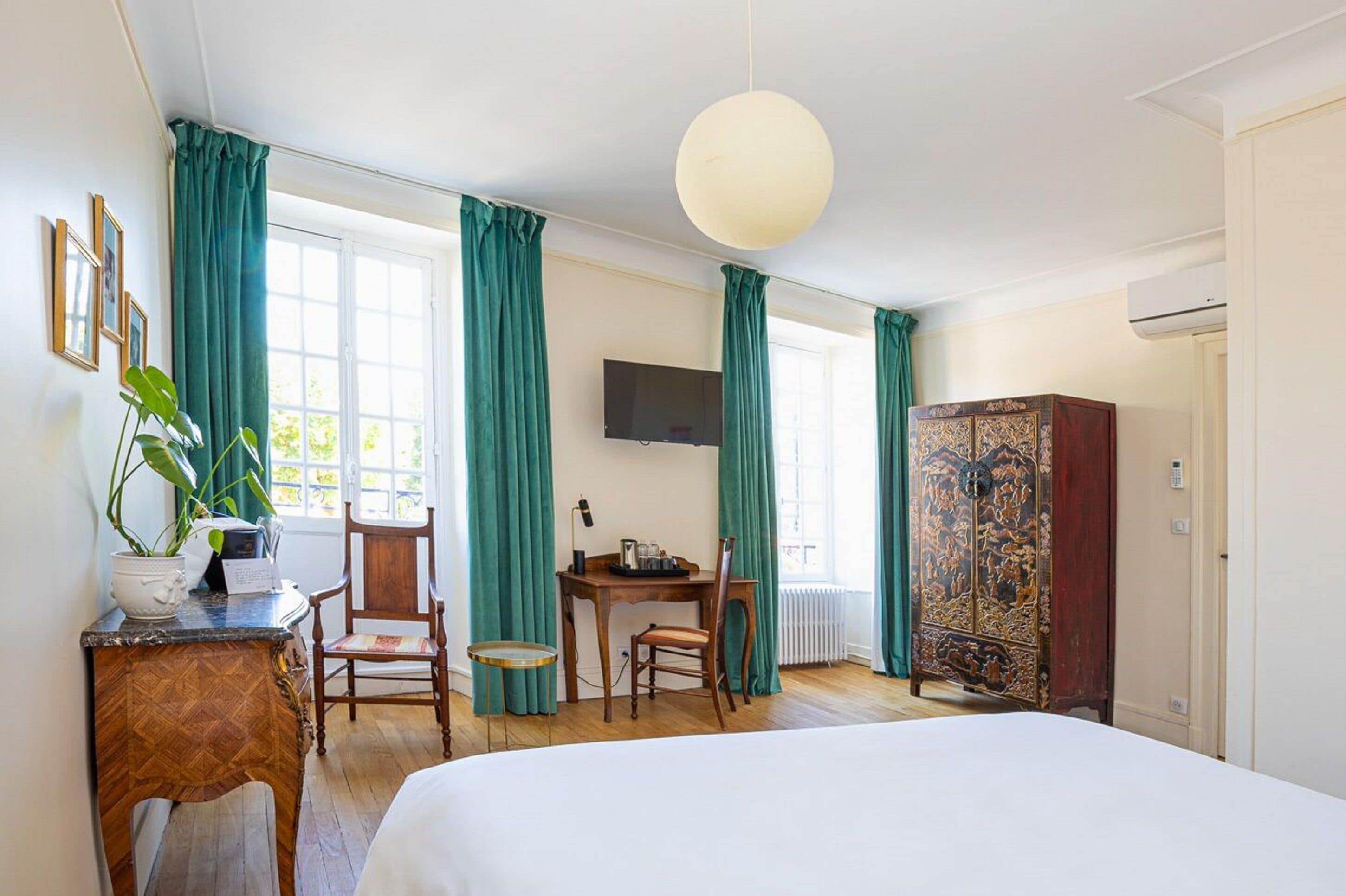 A hotel room with a bed, a desk with a chair, a television, and a cabinet.