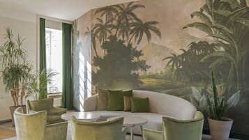 A room with a white sofa, green armchairs, a round table, and a large mural of tropical scenery.
