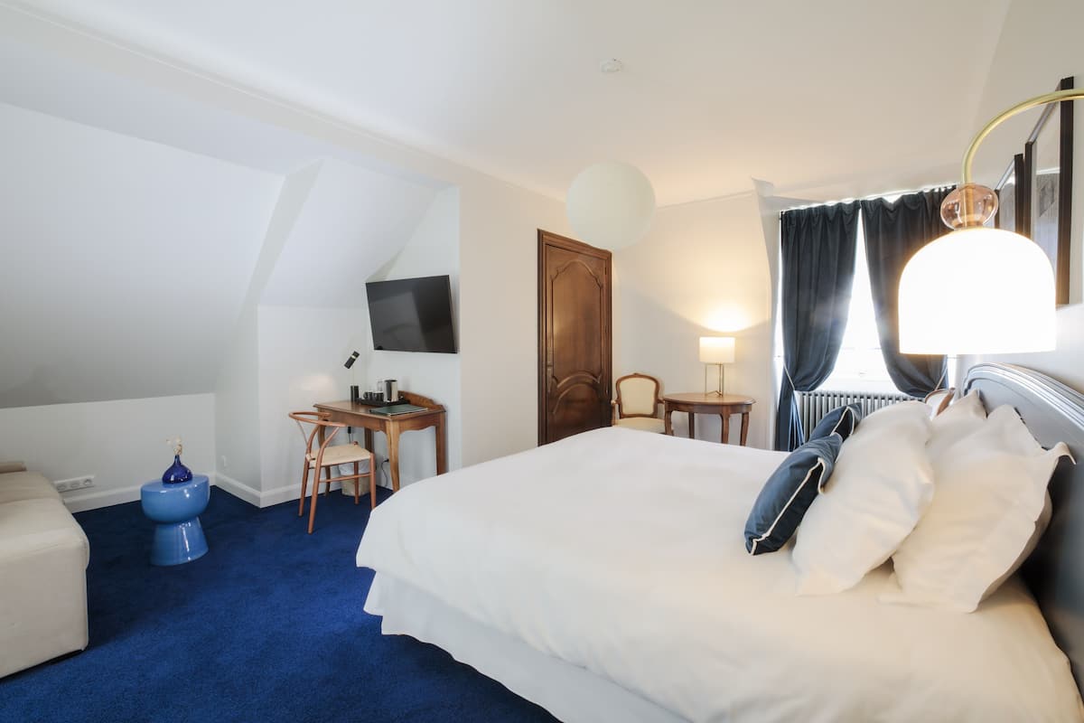 A hotel room with a large bed, a desk with a chair, a television mounted on the wall, and a window with curtains.