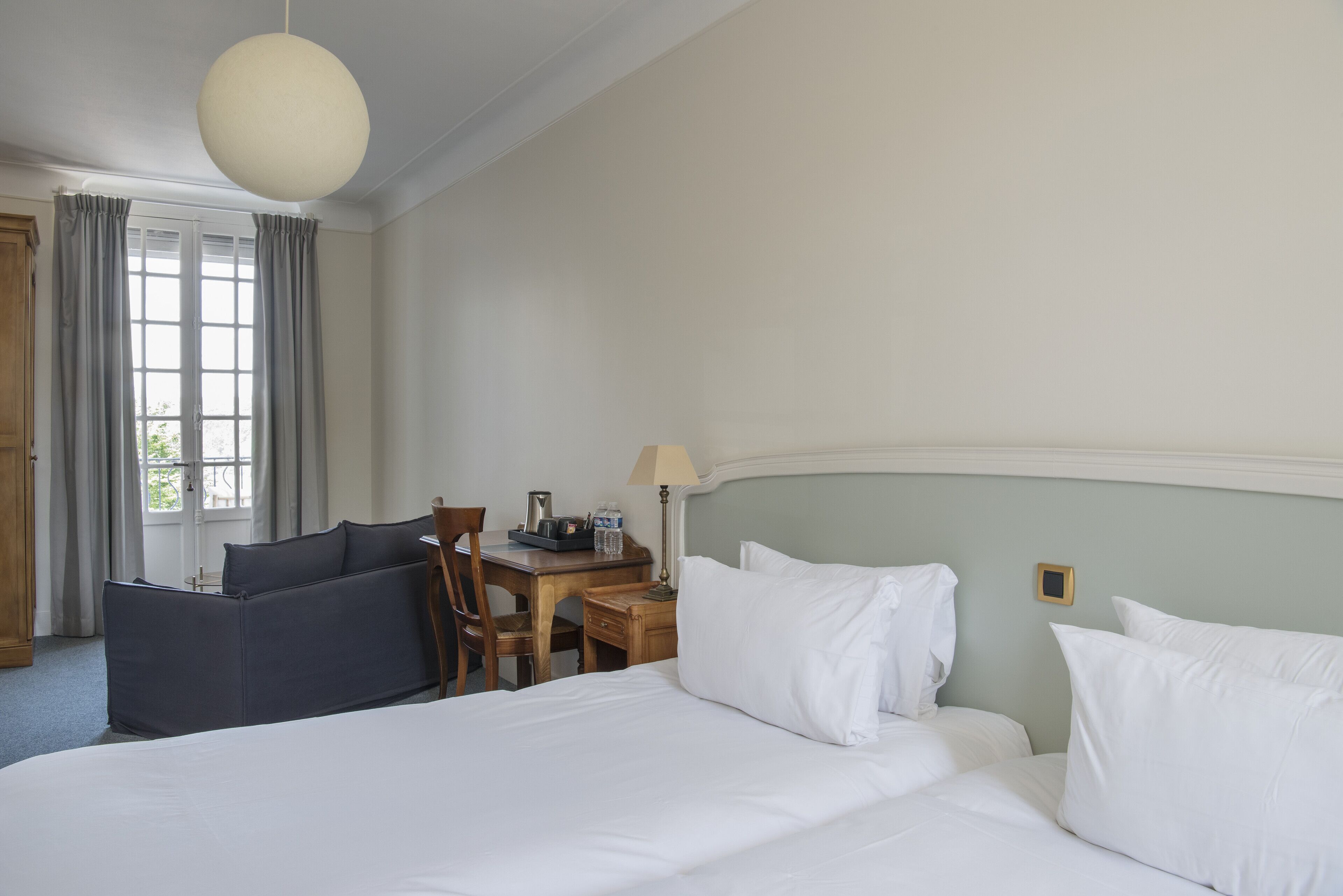 A hotel room with a bed, a desk, a chair, and a window with curtains.