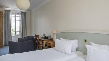 Una habitación de hotel con cama, escritorio, silla y ventana con cortinas.