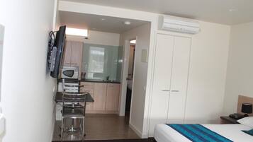 Quarto de hotel com cama, escrivaninha, cadeira, micro-ondas, pequena cozinha e guarda-roupa.