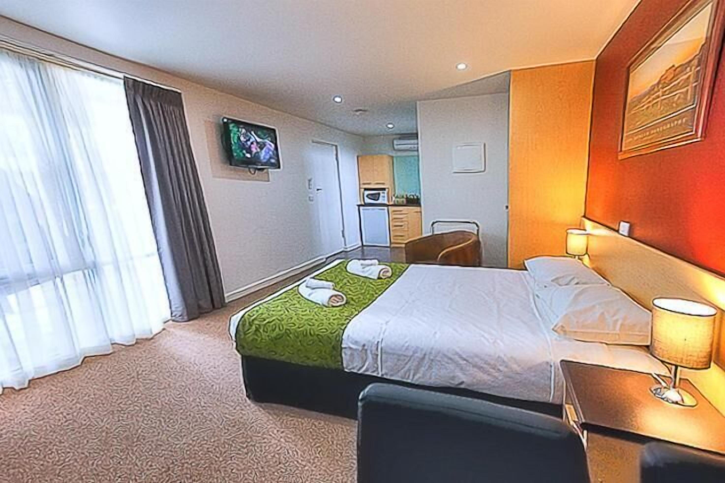 Une chambre d’hôtel avec un lit, un bureau, une chaise, une télévision et une fenêtre avec des rideaux.