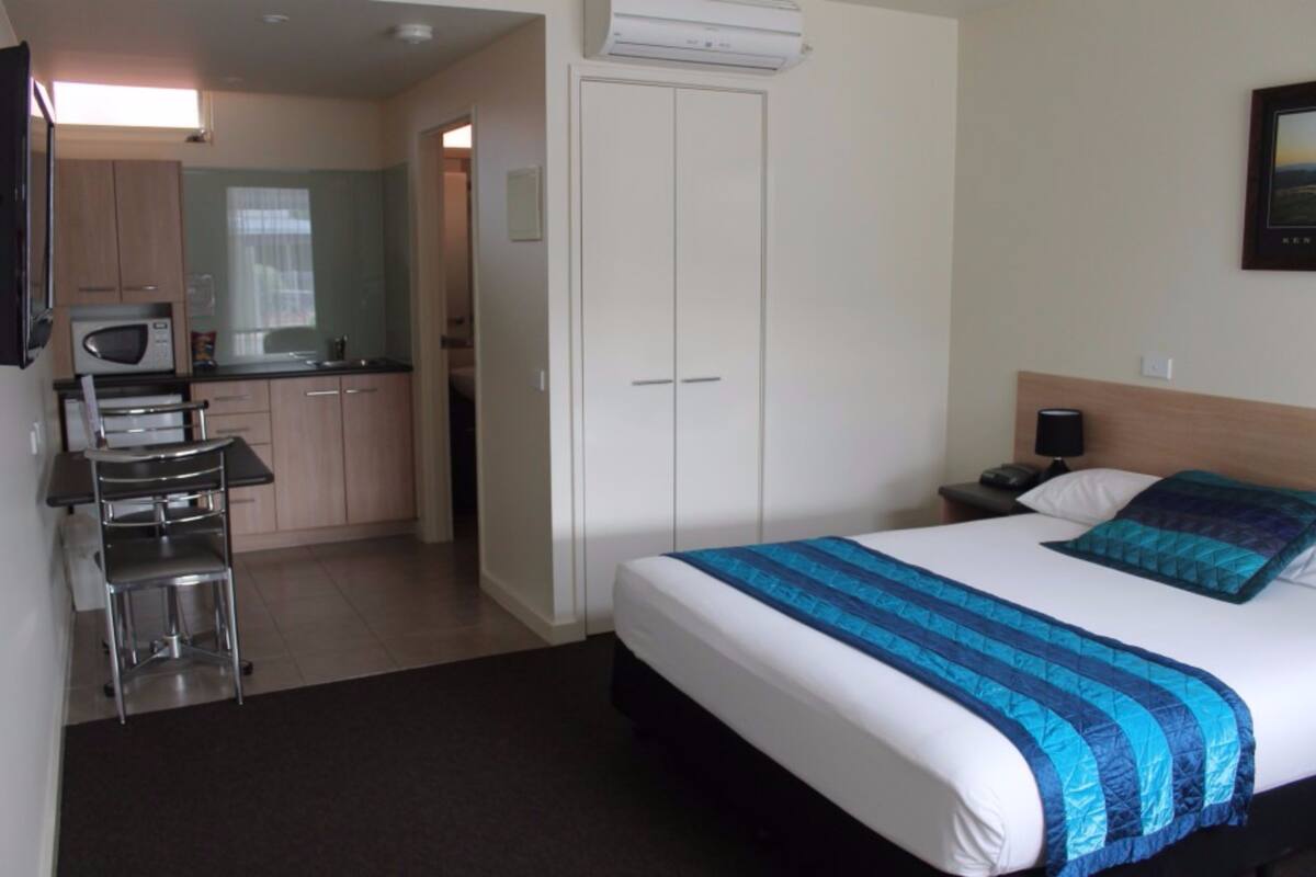 A hotel room with a bed, a desk, a chair, a microwave, a wardrobe, and a small kitchenette.